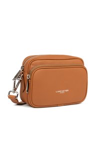 Borsa a tracolla in pelle marrone con due scomparti con zip, hardware argentato e logo impresso "LANCASTER PARIS" sul davanti.