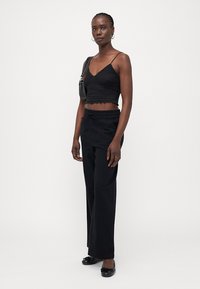 Must küllastatud knit tank top tekstuuriga disainiga, mis on ühendatud lõdva musta pükstega. Mudel kannab musti balletikingi ja hoiab käes väikest käekotti.