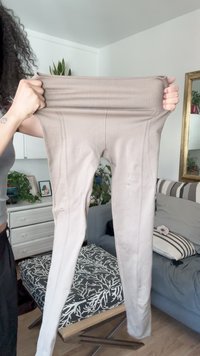 Beige høytliv leggings med ribbet liv, glatt tekstur, sømløs design og subtile sømdetaljer, holdt oppe mot en bakgrunn.