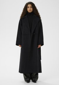 Palton lung negru din amestec de lână, cu un guler larg, mâneci supradimensionate și închidere cu un singur nasture. Textură netedă și design minimalist.