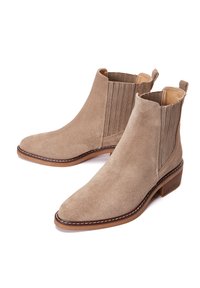 Bottines en daim beige avec des panneaux élastiques sur les côtés, un bout pointu et un petit talon empilé. Présente des coutures contrastantes autour de la semelle.