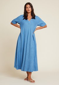 Blå, knelangen kjole laget av denimstoff med korte ermer og v-hals. Har en løs passform og subtil tekstur.