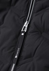 Tessuto trapuntato nero con una cerniera in metallo argentato e una linguetta di tiraggio nera con l'etichetta "Street One" cucita sul cursore della cerniera.