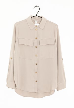 Beige long-sleeve button-up shirt with two chest pockets and gold buttons, displayed on a black hanger against a white background.
