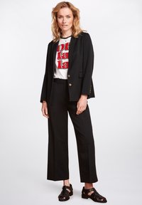 Svart skräddarsydd blazer med guldknappar, matchad med en vit t-shirt med grafik och svarta vida byxor, kompletterad med svarta sandaler med remmar.