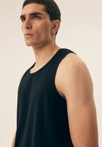 Black tank top in a smooth, lightweight fabric. Features a round neckline and wide armholes, showcasing a fitted silhouette.