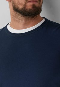 Marineblauw t-shirt met een ronde hals, voorzien van een witte binnenrand van de kraag. Glad textuur, eenvoudig ontwerp en korte mouwen.