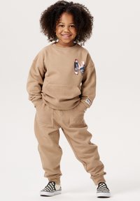 Beige Sweatshirt und Hose mit einer Fronttasche und gesticktem "N"-Logo; weiche Textur; kombiniert mit schwarz-weißen karierten Slippern.