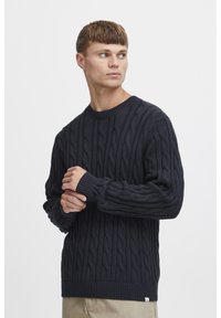 Marineblaue Strickpullover mit Rundhalsausschnitt, gerippten Bündchen und Saum, strukturiertem Muster und einem kleinen Etikett am unteren Rand.