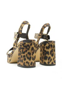 Sandalias de tacón alto con estampado de leopardo, con un tacón grueso y correa ajustable en el tobillo. El material presenta una textura suave con acentos en negro contrastantes.