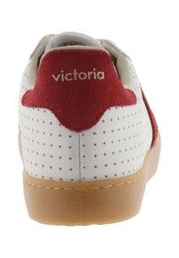 Witte sneaker met perforaties, gumzool en een rode suède hieltab met de opdruk "victoria" in gouden letters.