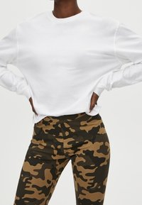 Witte trui met lange mouwen en ronde hals, gecombineerd met legging in bruin-zwart camouflagepatroon. De stof lijkt zacht en rekbaar.