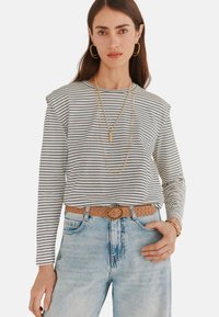 Stribet langærmet top i creme og marineblå, med skulderruffles. Sammen med lyseblå denimjeans og et vævet bælte. Gyldne hoop øreringe og lagdelte halskæder.