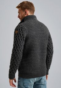 Suéter de punto gris oscuro con cuello alto, patrón texturizado en las mangas y dobladillo acanalado. Incluye un parche de marca en el hombro.
