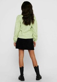 Hellgrüner Strickpullover mit voluminösen Ärmeln, kombiniert mit einem schwarzen Wildleder-Minirock und schwarzen Stiefeletten, Rückansicht.