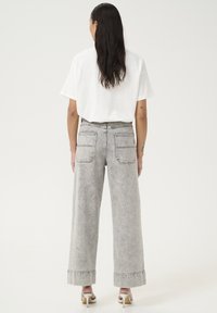 Grå bredbenede jeans med høj talje, baglommer og opsmøgte ben, parret med en løs hvid t-shirt, omridsende mod en hvid baggrund.