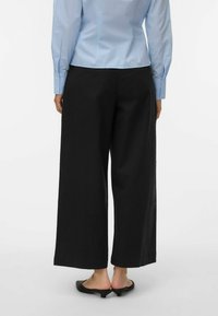 Pantalones negros de pierna ancha hechos de tela ligera, con una textura suave y bolsillos laterales, combinados con una camisa abotonada de color azul claro.