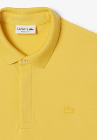 Gul Lacoste pikétröja med en texturerad tyg, en klassisk krage, en tvåknappslåsstängning och en broderad krokodil-logotyp på bröstet.