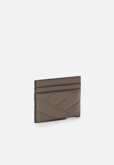 Porte-cartes en cuir matelassé de couleur gris pâle, avec un motif de couture en diagonale, quatre emplacements pour cartes et un profil mince pour un transport facile.