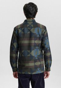Camicia a fantasia in tonalità di verde scuro, blu e marrone; presenta forme geometriche e polsini con bottoni; realizzata in tessuto testurizzato.
