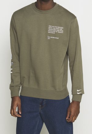 Sweatshirt vert olive avec du texte blanc sur le devant et la manche. Tissu doux, col rond, poignets côtelés, et logo Nike brodé sur la manche.