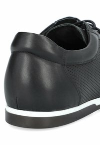 Czarne perforowane skórzane buty z zaokrąglonym tyłem, z białą podeszwą środkową i ciemną gumową podeszwą. Sznurowane przez oczka z przodu.
