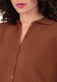 Cardigan marron texturé avec col, fermeture à boutons et tissu doux. Doté de boutons ronds le long de la patte de boutonnage avant.