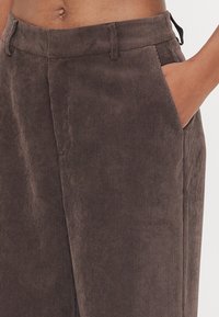 Bruine corduroy broek met een gemêleerd verticale streep patroon, voorzien van zijzakken en een ontspannen pasvorm. Subtiele stikdetails bij de taille.
