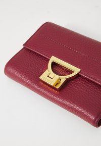 Portafoglio in pelle bordeaux con superficie texture, dotato di una chiusura in metallo dorato e dettagli di cucitura lungo i bordi.