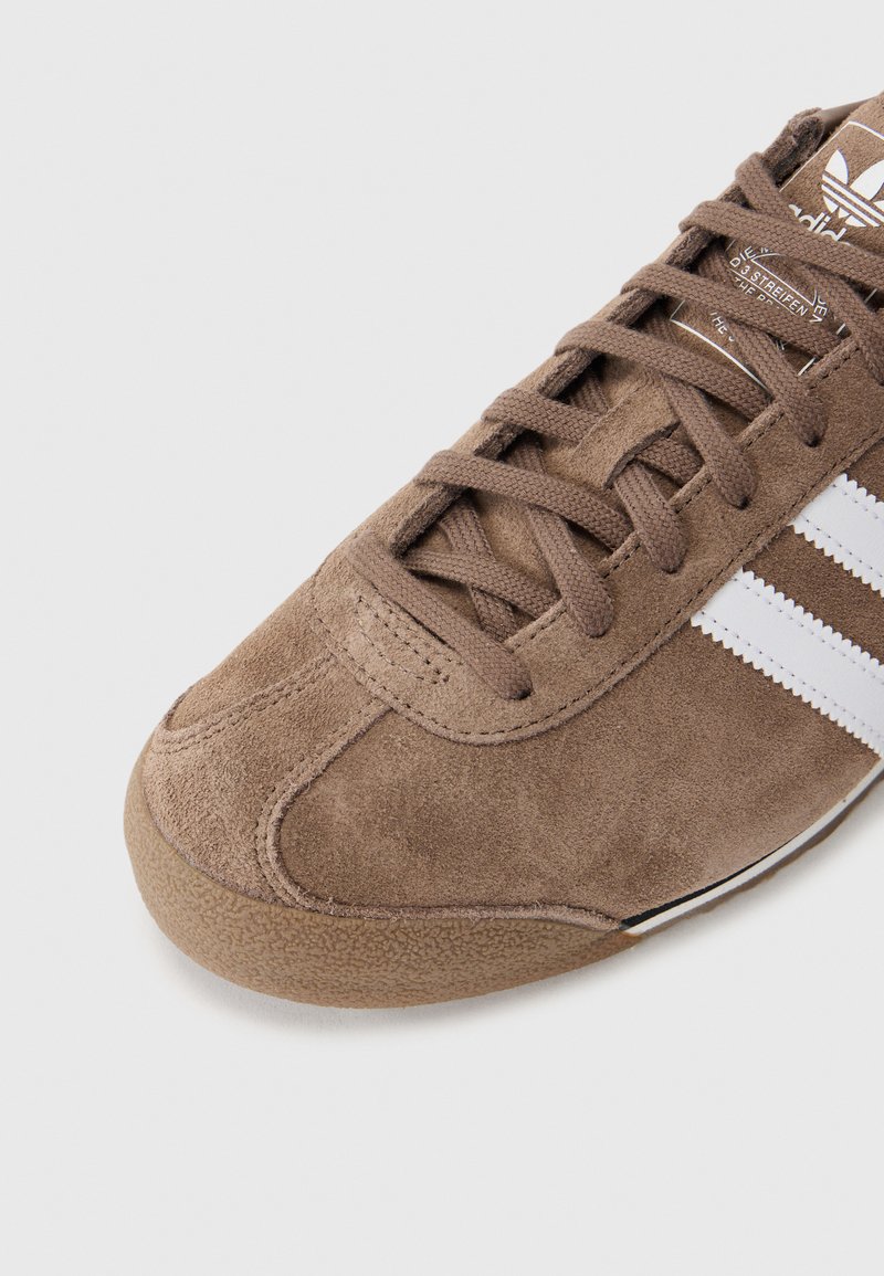 Bottines de sport en daim marron avec des rayures latérales blanches, bout rond et semelle en caoutchouc texturé ; fermeture à lacets avec lacets plats.