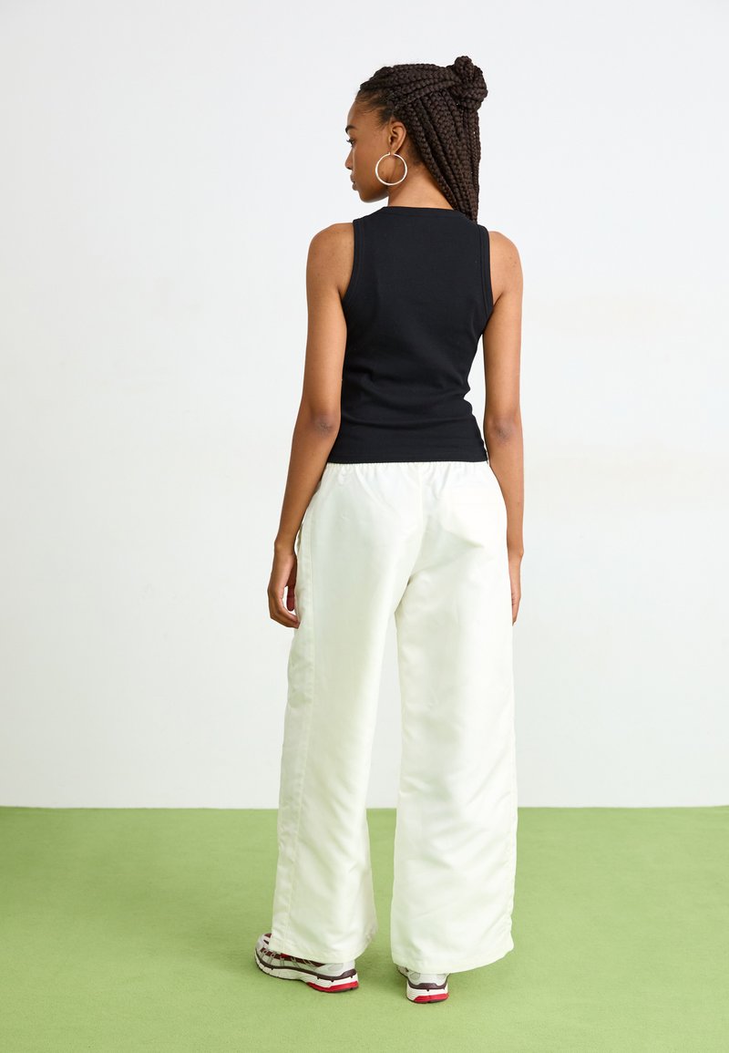 Top noir sans manches associé à un pantalon large blanc ; tissu lisse avec une taille élastique. Design simple, couleurs neutres et coupe décontractée.