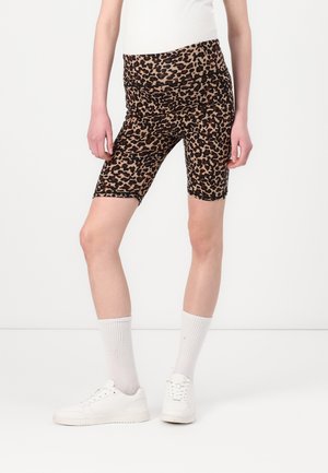Person iført højtaljede biker shorts med leopardprint, hvide crew-sokker og hvide sneakers, stående mod en ensartet lys baggrund.
