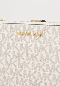 Borsetta bianca con tessuto texturizzato che presenta un motivo a monogramma ripetuto. Accenti in metallo dorato per il logo e la cerniera.