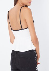 Top peplum blanco con ribete negro, tirantes finos y espalda descubierta. Combinado con jeans negros que tienen adornos de perlas en los laterales.