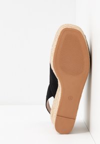 Espadrille noire avec un talon compensé en jute tressé et une semelle en caoutchouc. Présente un design découpé sur le côté et une étiquette de taille "37" sur la semelle.