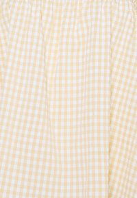 Żółto-białą tkanina w kratkę o lekkiej teksturze i marszczonej elastycznej talii, tworząca miękki, płynny wygląd.