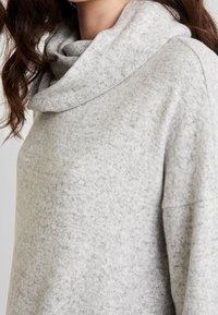 Grauer Pullover mit Schlupfkragen aus weichem, strukturiertem Stoff, mit lockerer Passform und abgesenkten Schultern. Dezentes, gesprenkeltes Muster im gesamten Pullover.