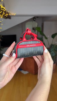 Mini-Handtasche mit einem schwarzen, strukturierten Körper, roten Akzenten und zwei oberen Griffen. Logo ist gut sichtbar auf der Vorderseite angebracht. Reißverschlussverschluss.