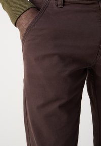 Καφέ βαμβακερό παντελόνι με λεία υφή, που διαθέτει εμπρόσθιες τσέπες και λεπτομερή ραφή κατά μήκος των ραφών.