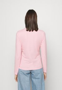 Ljusrosa långärmad skjorta i mjukt tyg med en figurnära passform och rund halsringning, i kombination med ljusblå denimbyxor.