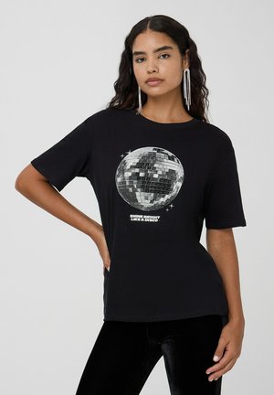 T-shirt nera con grafica di una palla da discoteca argentata e testo "BRILLA FORTE COME UNA DISCO." Maniche corte e vestibilità rilassata, in materiale cotone.