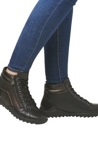 Chaussures montantes noires en cuir texturé, avec une fermeture éclair sur le côté, des accents métalliques et une semelle robuste, associées à un jean bleu.