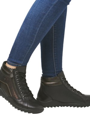 Chaussures montantes noires en cuir texturé, avec une fermeture éclair sur le côté, des accents métalliques et une semelle robuste, associées à un jean bleu.