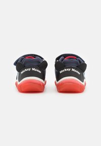 Zapatillas azul marino con acentos rojos, que cuentan con orejas y logo de Mickey Mouse en el talón. Diseñadas con una correa de velcro para facilitar su uso.