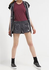 Idrottskläder bestående av en mörkröd t-shirt med rund hals, svarta mönstrade shorts med dragkedjor och svarta sneakers med vita sulor.