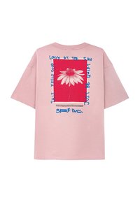 Różowa bawełniana koszulka z krótkim rękawem, z grafiką z przodu przedstawiającą białą stokrotkę na czerwonym tle z niebieskimi akcentami tekstowymi.