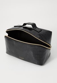 Neceser de cocodrilo negro con relieve y cremallera dorada, forma rectangular plana, asa superior y interior oscuro. Presenta detalles de la marca.