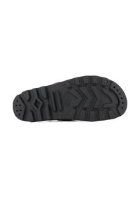 Semelle en caoutchouc noir avec des crampons profonds et des motifs de traction prononcés. Présente des zones texturées et des trous de ventilation pour une meilleure adhérence et circulation de l'air.