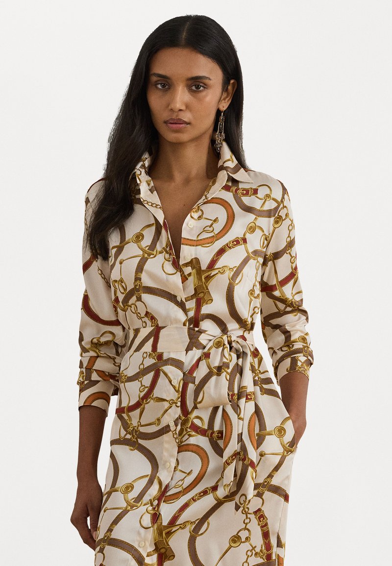Abito lungo con colletto realizzato in tessuto beige con un motivo a catena dorata e rossa. Include una vita legata e chiusura con bottoni, con maniche arrotolabili.