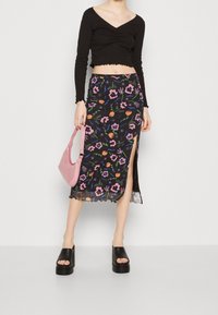 Svart långärmad crop top med v-ringning; blommönstrad midikjol i svart, rosa och orange; rosa handväska; kraftiga svarta plattformsskor.